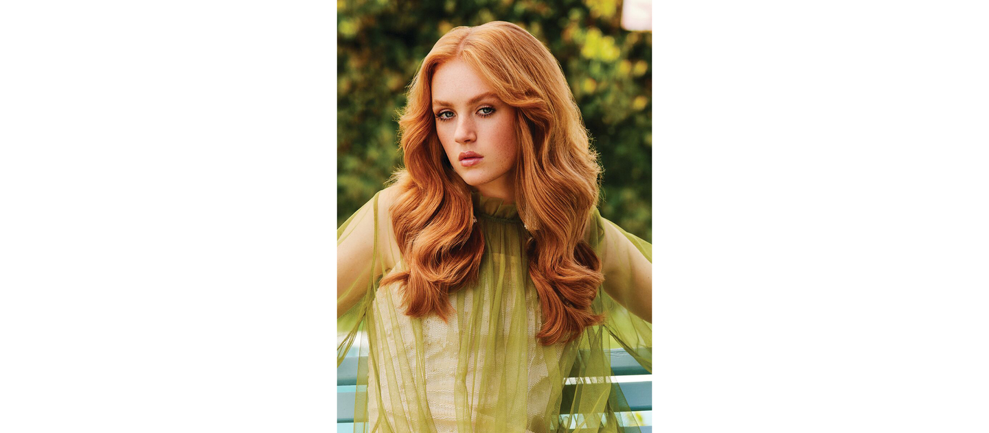 Red-haired woman with soft, flowing curls draped over a sheer lime green top, showcasing a simple yet elegant hairdo.